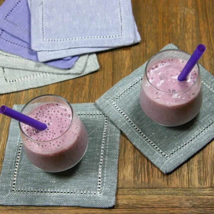 two small strawberry blueberry banana smoothies on napkins with straws