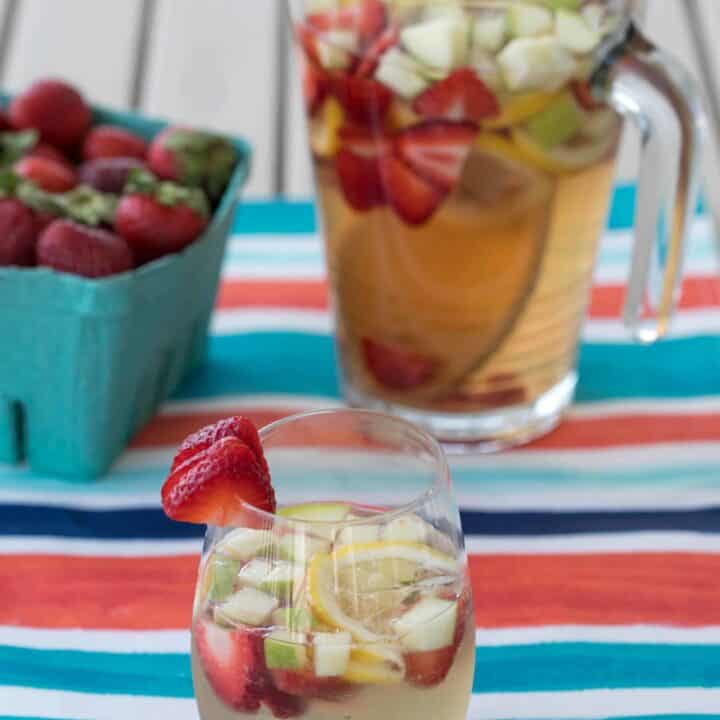white wine sangria in a cup and a pitcher with strawberries, green apple, and lemon