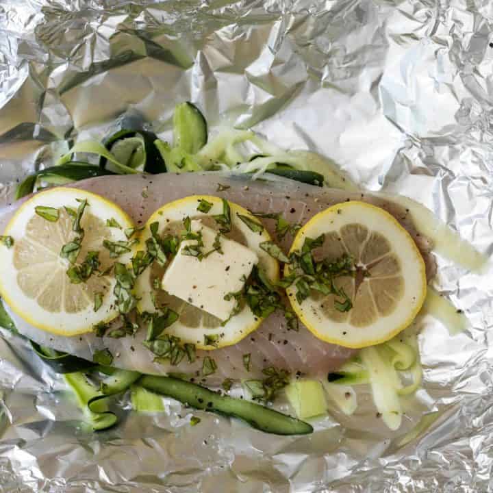 tilapia fillet on tin foil with shaved zucchini ribbons, butter, and lemon slices