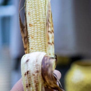 hand holding ear of grilled corn with husk pulled back