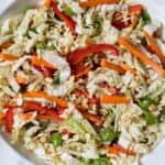 asian cabbage slaw with napa cabbage, red peppers, snow peas, and carrots with asian dressing in a large white bowl