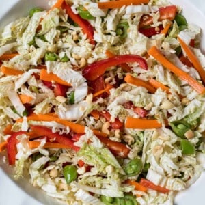 asian cabbage slaw with napa cabbage, red peppers, snow peas, and carrots with asian dressing in a large white bowl