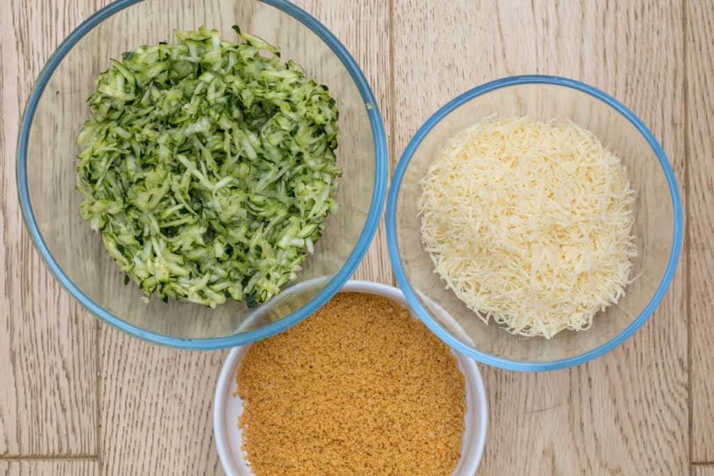 bowls of ingredients for zucchini gratin: shredded zucchini, cheese, and seasoned breadcrumbs