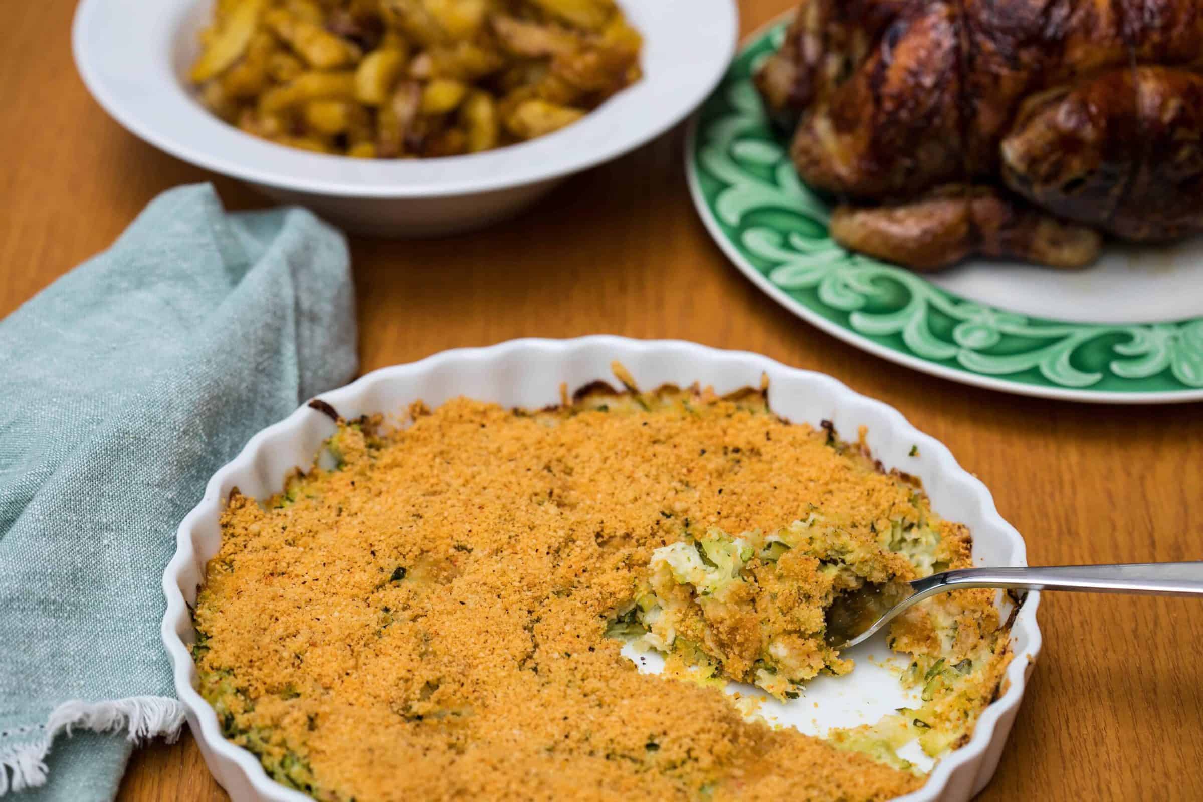 zucchini gratin with green napkin, and roasted potatoes and chicken on plates in background