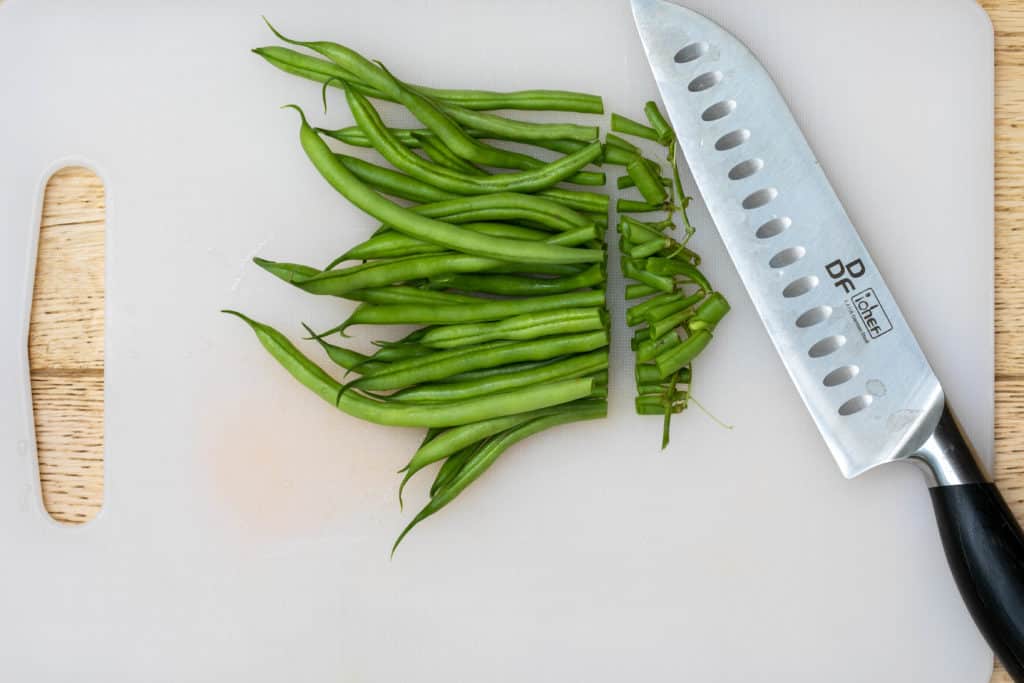 Trimming green beans on cutting board with knife