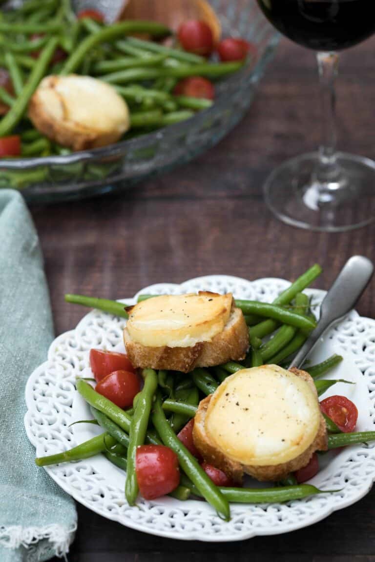 green bean salad with goat cheese toasts on white plate with napkin and platter and glass of wine in background