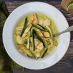bowl of chicken curry with coconut milk and zucchini with green napkin and lime slices