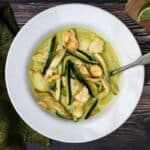 bowl of chicken curry with coconut milk and zucchini with green napkin and lime slices on cutting board