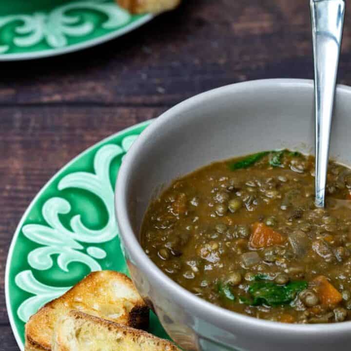 bowl of French lentil soup with baguette toasts in brown bowl on green plate