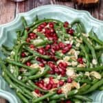 green beans almondine with pomegranate seeds in large platter with seeds and tongs