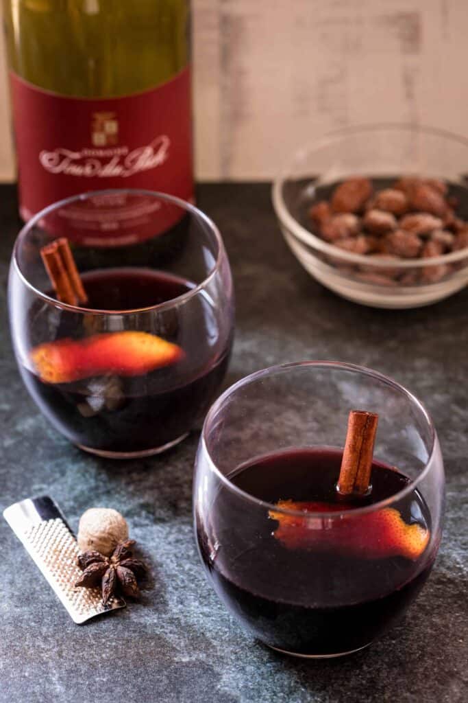 two glasses of vin chaud with wine bottle and nuts in background