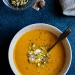 carrot ginger soup with small bowl of pistachios, nutmeg, and napkin