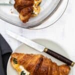 croissant breakfast sandwich on plate with knife and napkin and baking dish