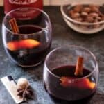 two glasses of vin chaud with wine bottle and nuts in background