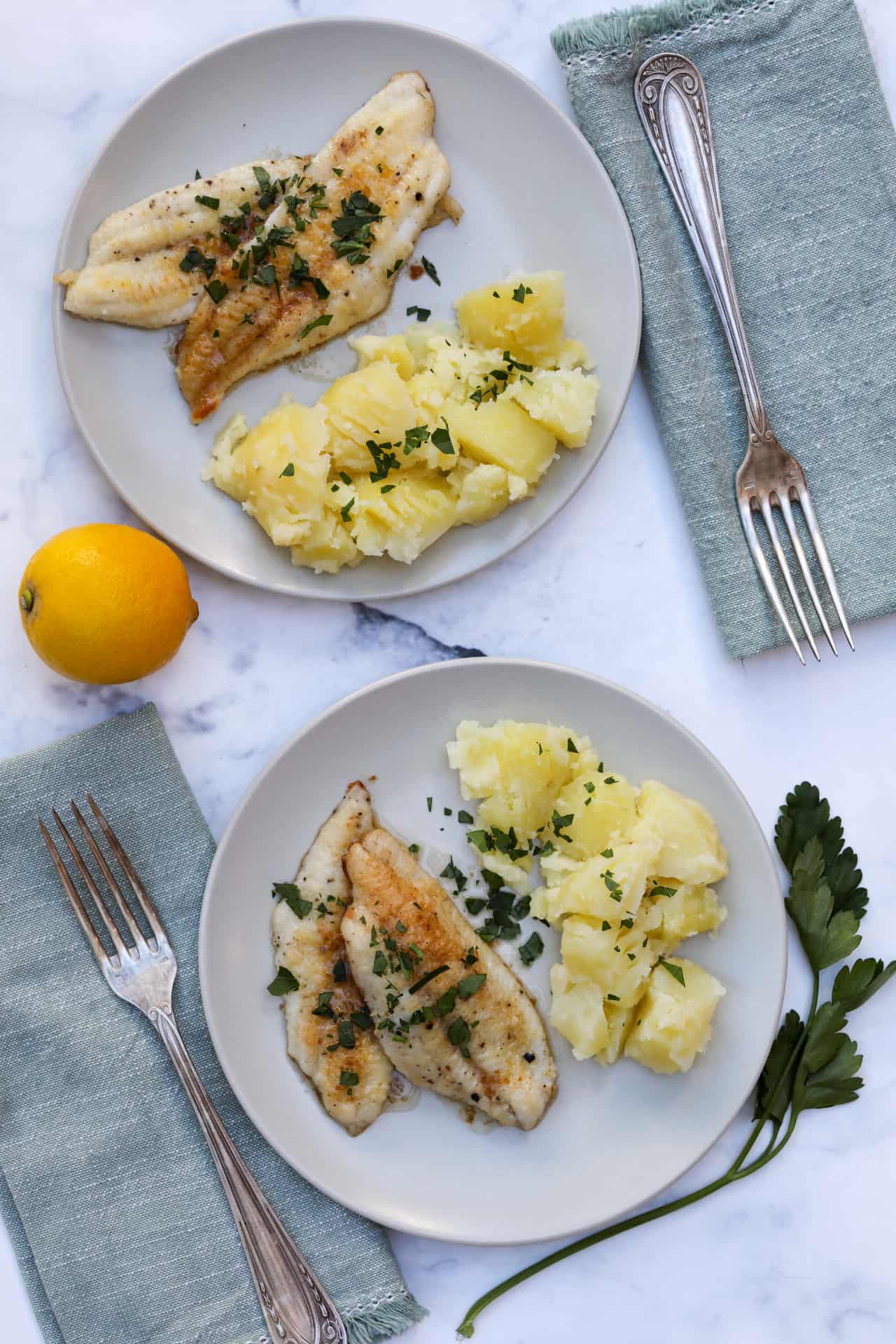Sole meuniere on two plates with forks, napkins, parsley and lemon