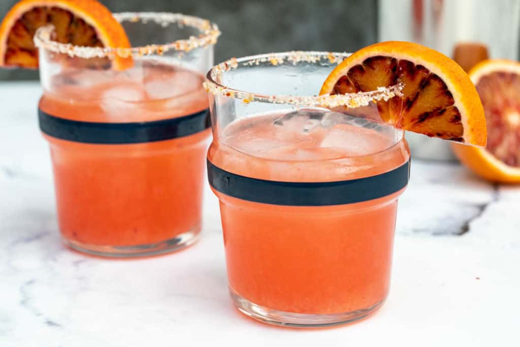 two glasses of blood orange margaritas with shaker in background
