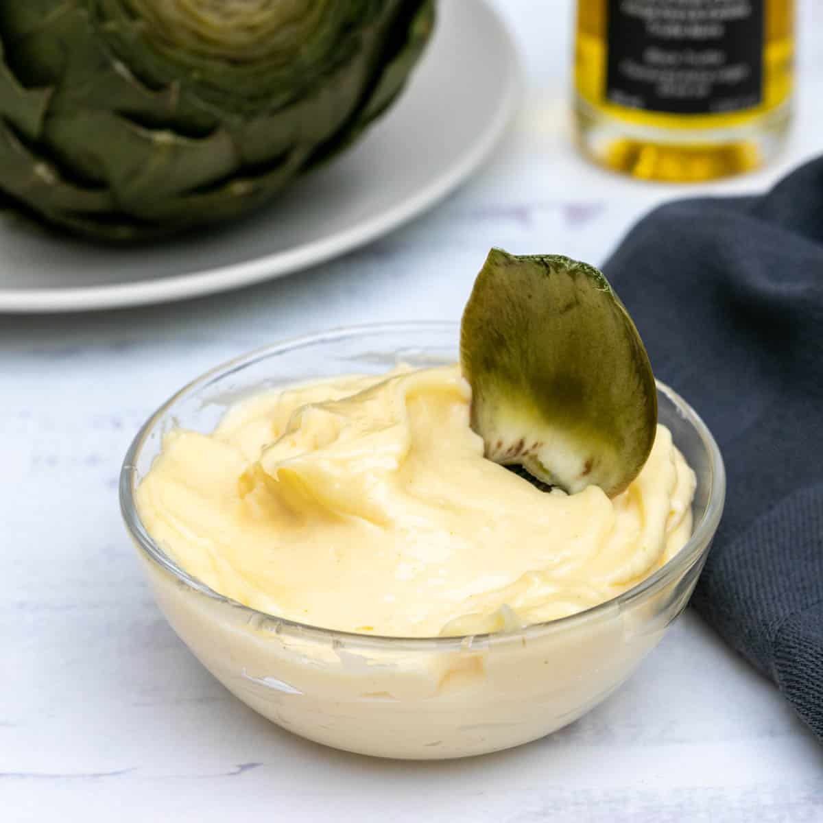 small bowl of truffle aioli with artichoke in background