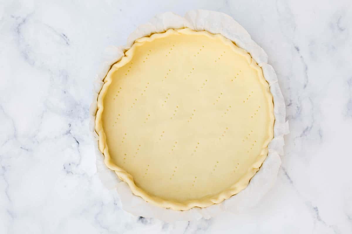 pie crust lined with parchment paper in quiche pan