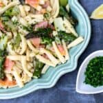 close up of smoked salmon and asparagus pasta on platter with lemon wedge and small bowl of chives