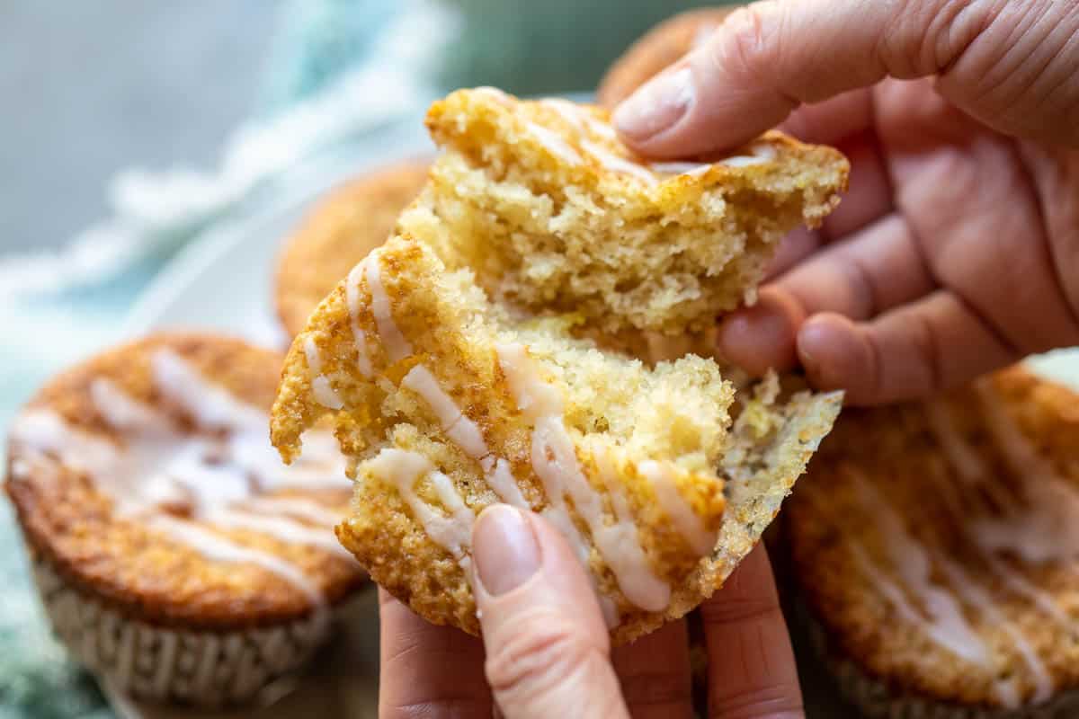 hands breaking almond flour muffin in half with other muffins in background