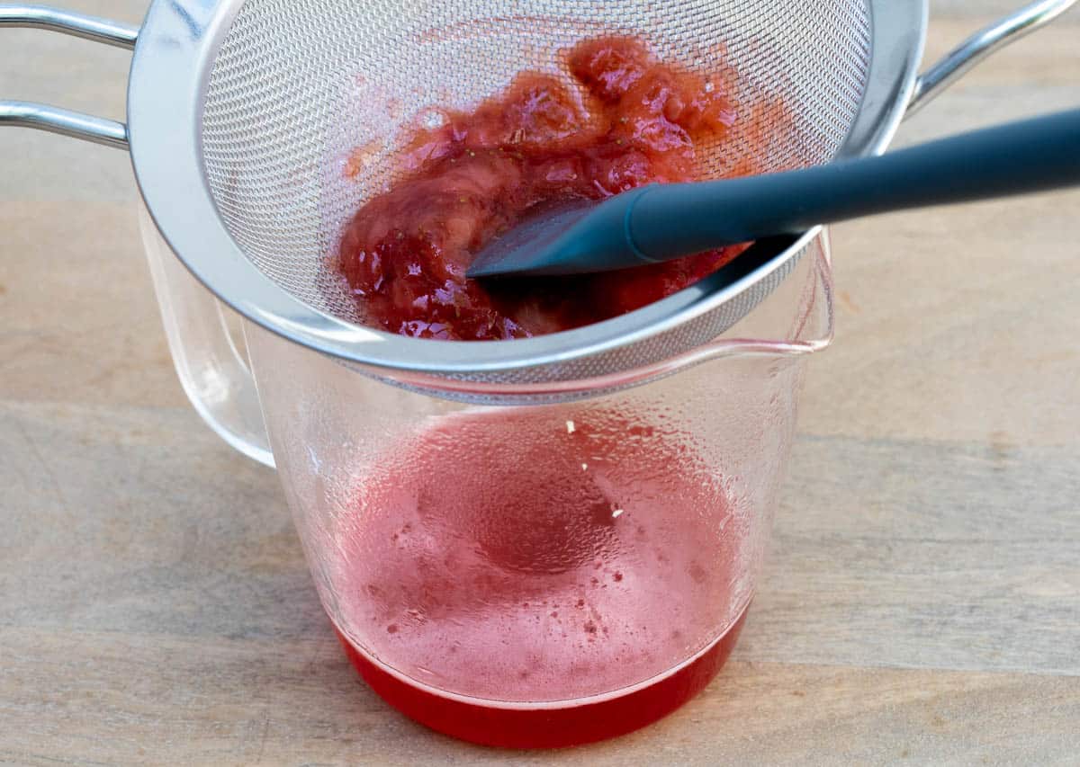 straining strawberry syrup into glass measuring cup