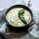 bowl of pesto aioli with basil leaf on green napkin