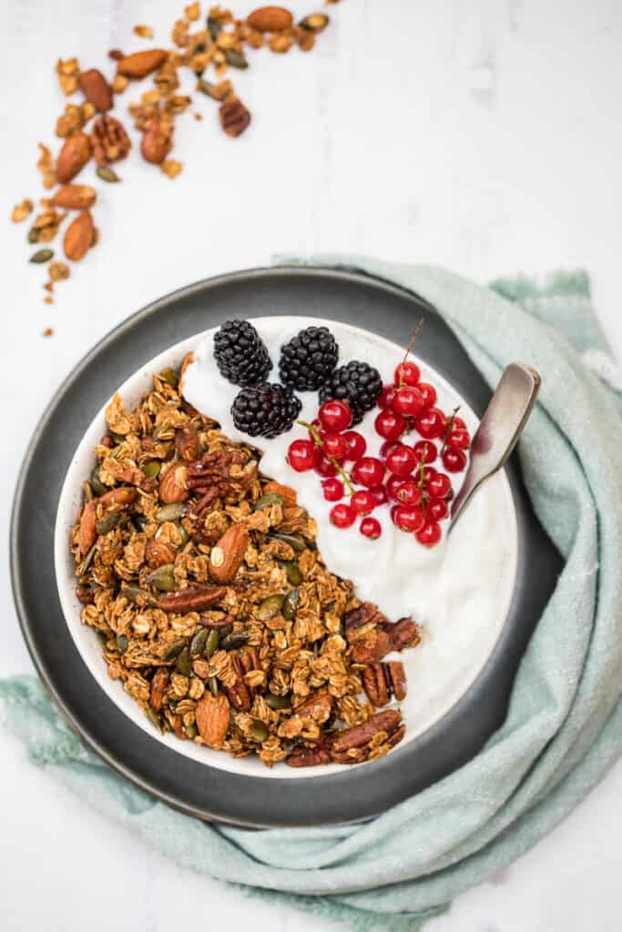 bowl of granola and yogurt with berries with green napkin and spilled granola in the background