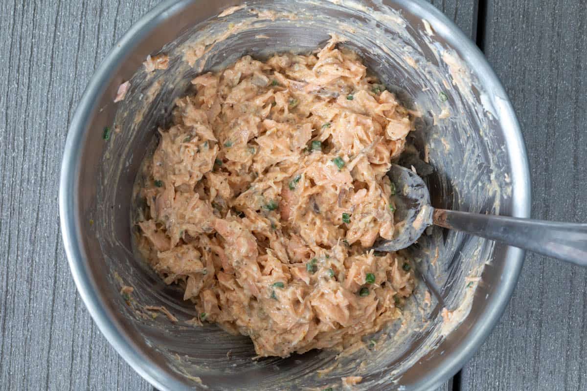 Old Bay butter mixture mixed with cooked salmon in metal bowl