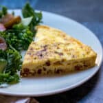 close up of slice of crustless quiche lorraine on small plate with salad