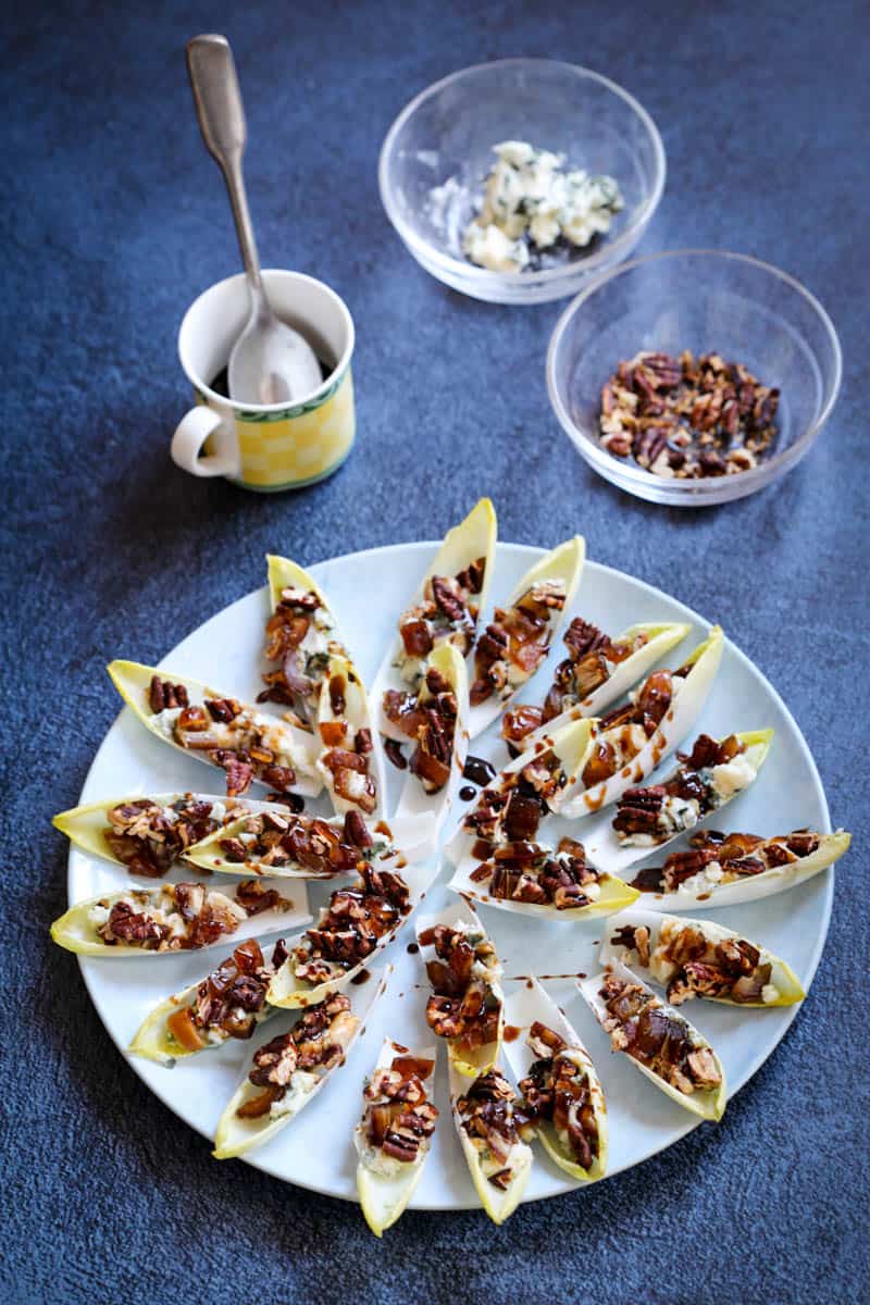 Blue cheese and pecan endive appetizer on serving plate with bowls of blue cheese and pecans in background