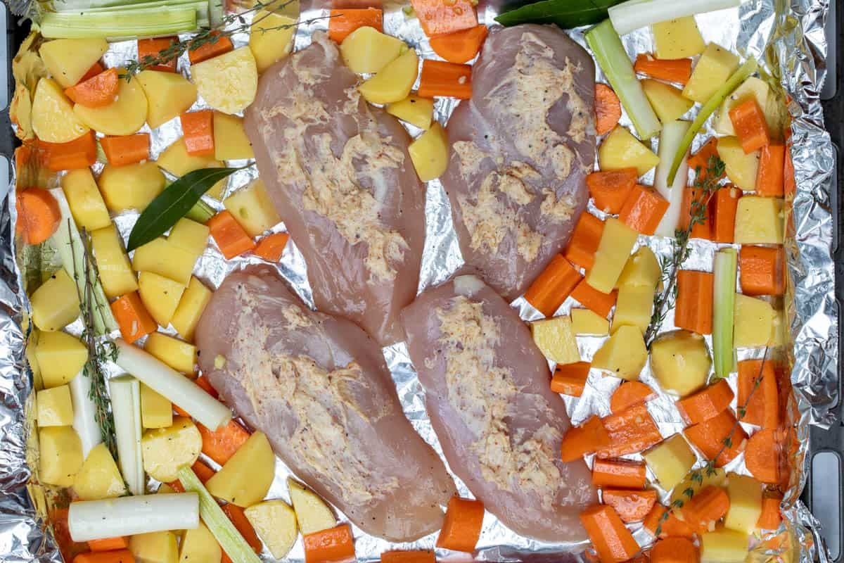 chicken breasts with spiced butter on foil lined sheet pan with potatoes, carrots, leeks and herbs