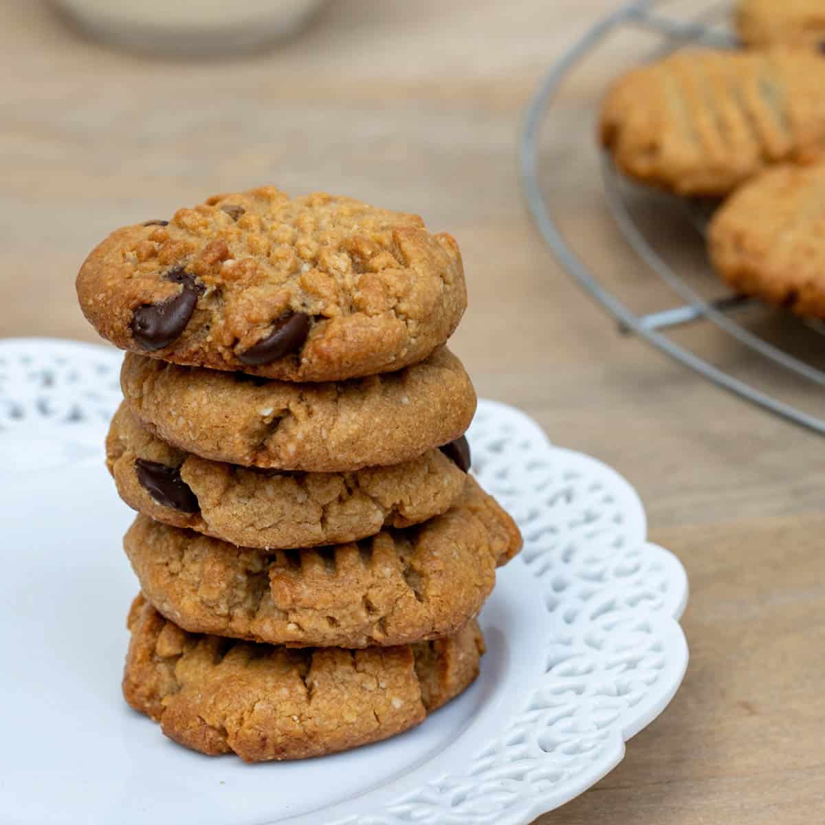 stack of almond flour peanut butter cookies on a plate with cookies on rack behind them