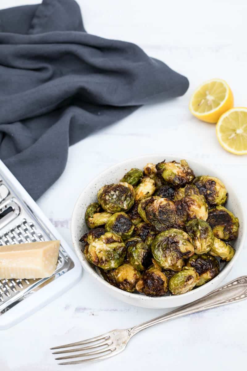 smashed brussels sprouts in bowl with lemon and parmesan cheese and fork and napkin