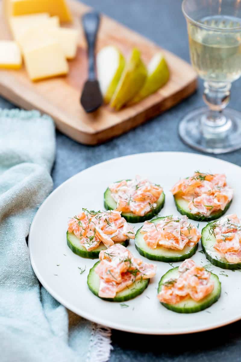 plate of smoked salmon canapés with cucumber with napkin, glass of wine, and cutting board in the background