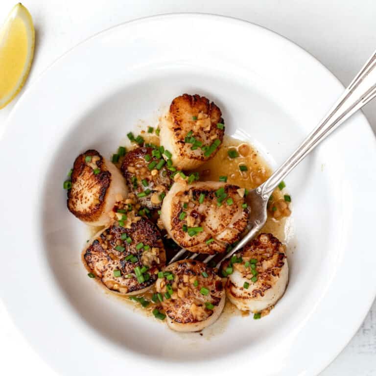 bowl of spicy scallop scampi with fork and lemon wedge