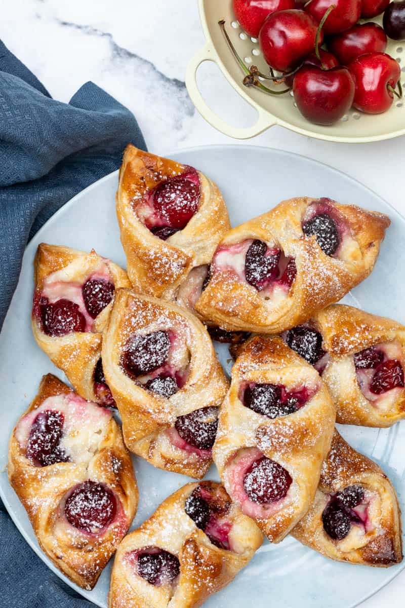 plate of cherry danishes next to napkin and colander with fresh cherries
