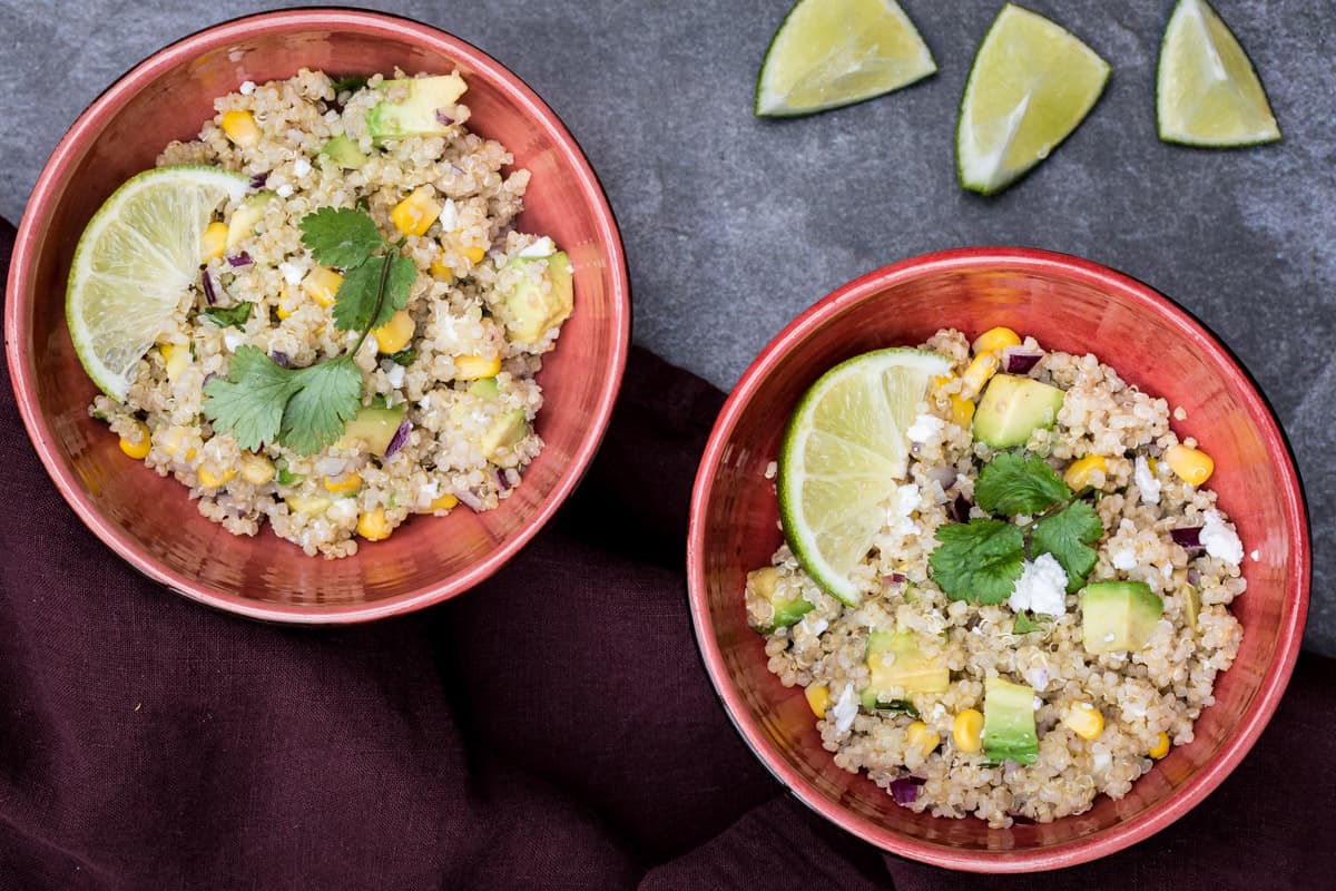 two small bowls of quinoa avocado salad with lime wedges and napkin