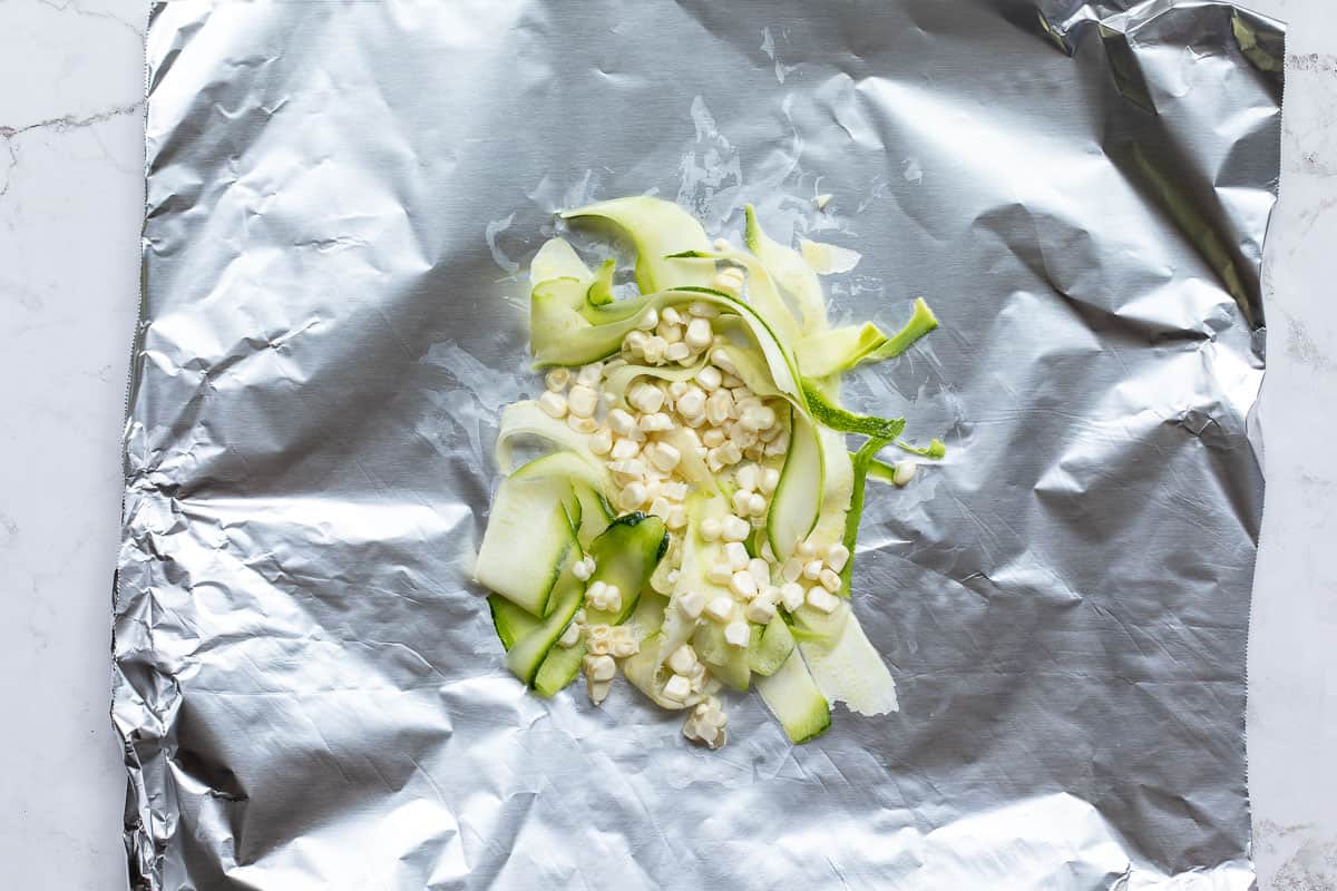 pile of zucchini ribbons and corn kernels on piece of aluminum foil.