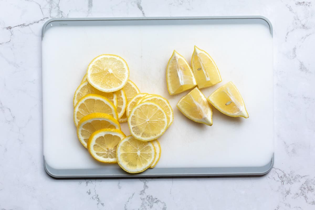 sliced lemons on cutting board next to lemon wedges.