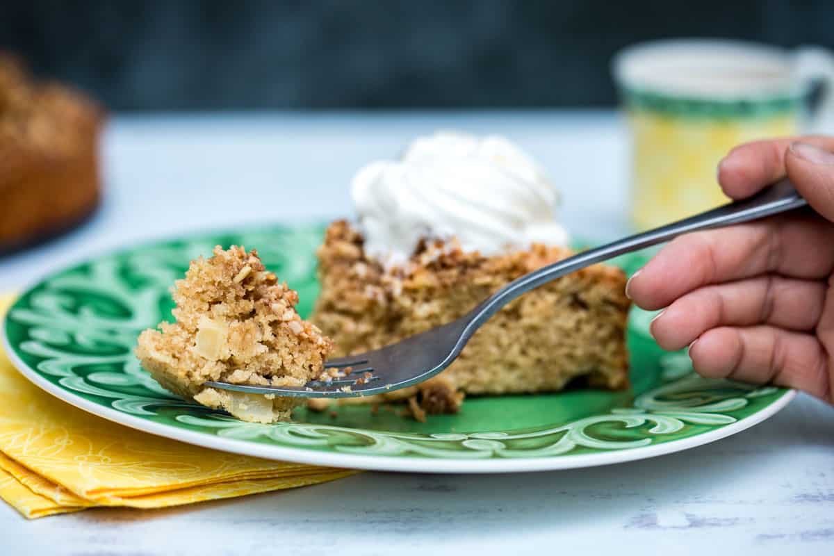slice of apple almond cake on a plate with fork holding one bite of cake on it
