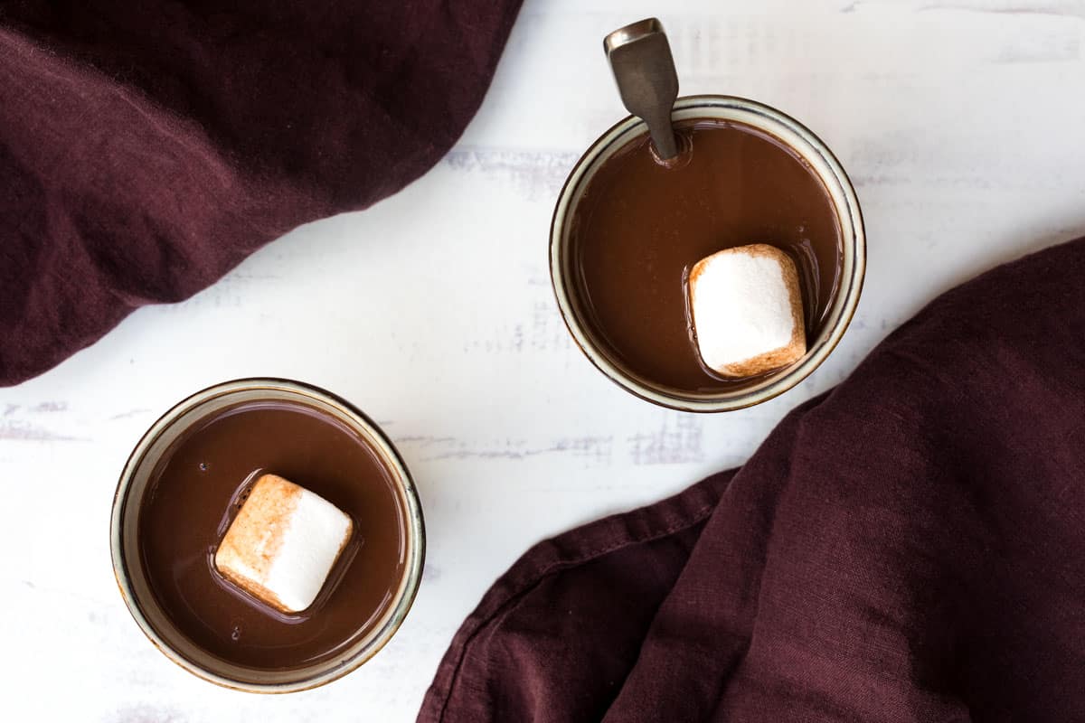 two mugs of oat milk hot chocolate next to purple napkins