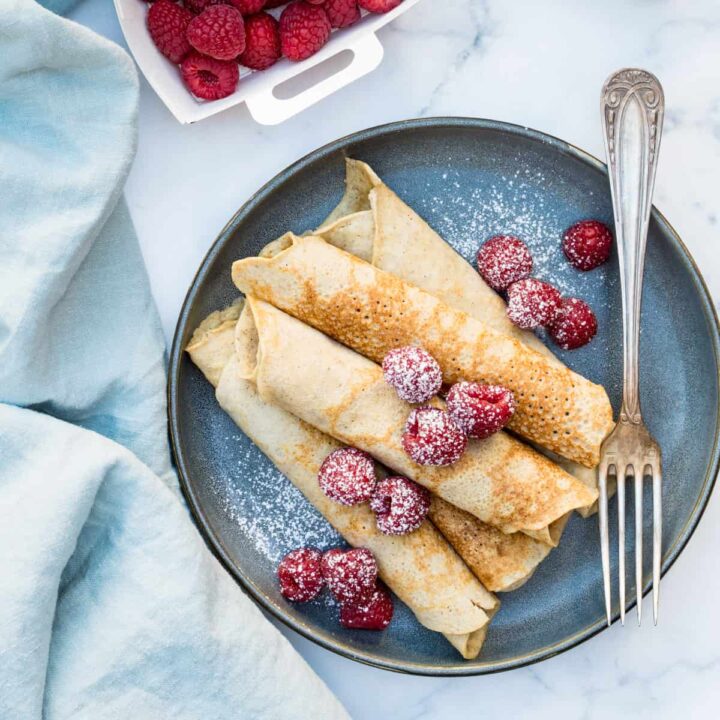 plate of gluten-free crepes with almond flour on plate with raspberries, fork and napkin