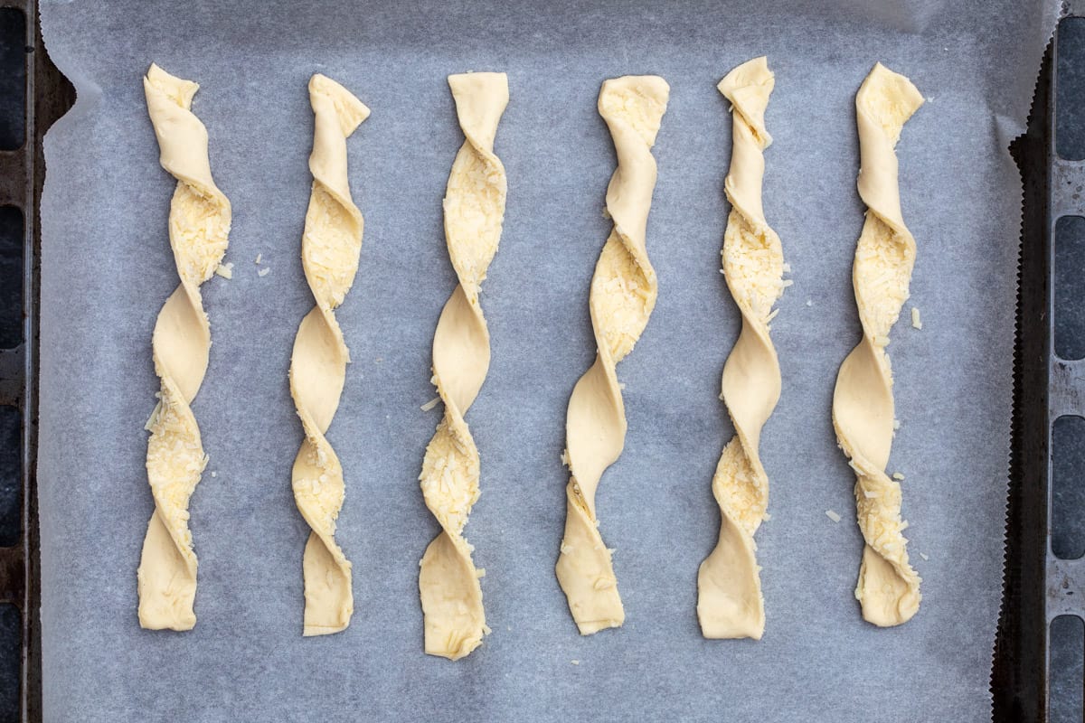 unbaked puff pastry cheese straws on parchment-lined baking sheet