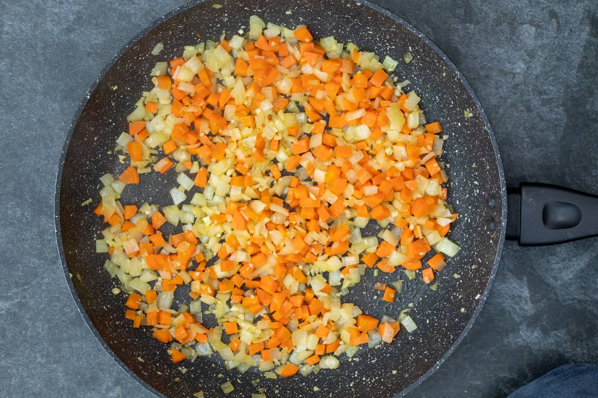 large skillet with sautéed onion, carrots, and garlic