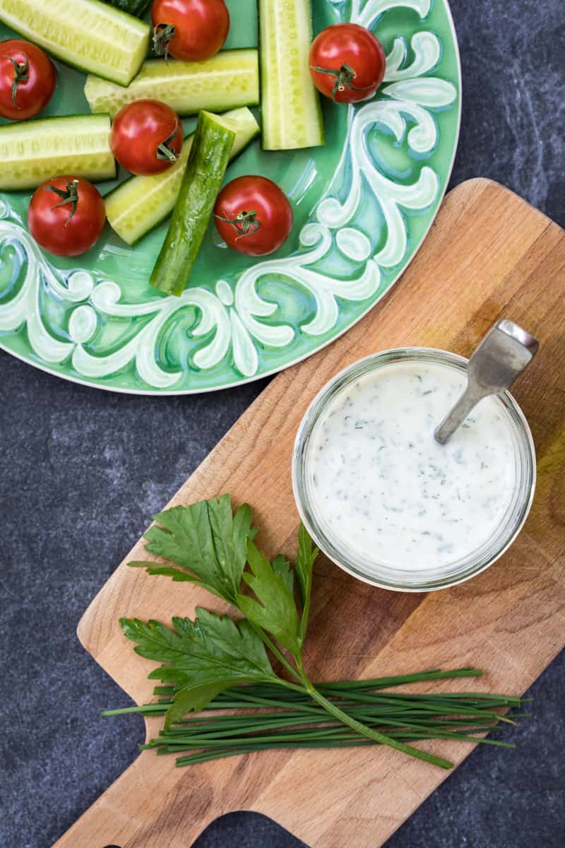jar of healthy ranch dressing next to plate of tomatoes and cucumbers and fresh herbs
