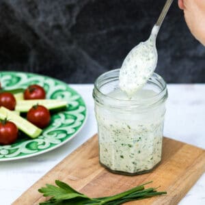 healthy ranch dressing in jar with spoon next to plate of vegetables