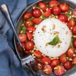 close up of burrata with tomatoes and pesto with serving fork and napkin