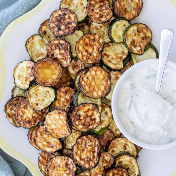 air fryer zucchini coins on plate with bowl of sour cream dip