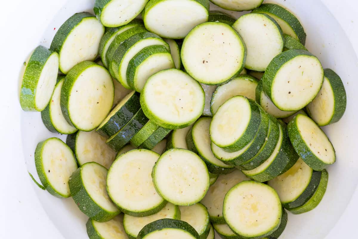 zucchini coins in large bowl tossed with olive oil, salt, and pepper