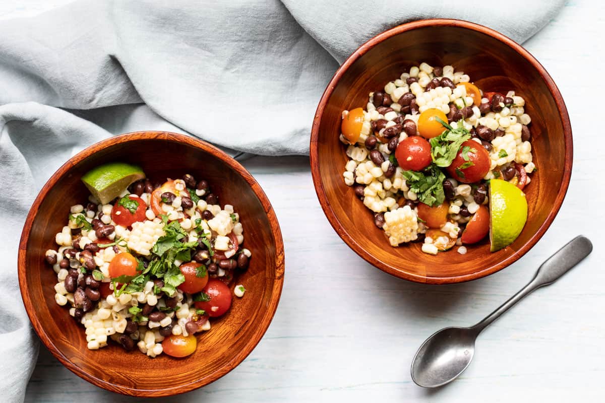 two small bowls of black bean and corn salad with napkin and spoon